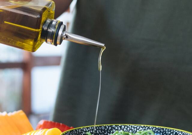 Person Pouring Liquid on Green Noodles in Ceramic Bowl