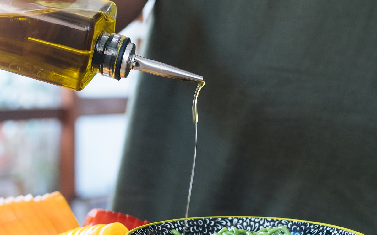 Person Pouring Liquid on Green Noodles in Ceramic Bowl